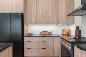 A modern kitchen with wooden cabinets, a black refrigerator, and a wooden fish-shaped cutting board. - Pelican Lake Getaway, 2BR + Office, Beach & Pedal Boat (Breezy Point)