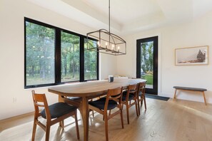 A modern dining area with a wooden table and chairs, large windows, and a hanging light fixture. - Pelican Lake Getaway, 2BR + Office, Beach & Pedal Boat (Breezy Point)