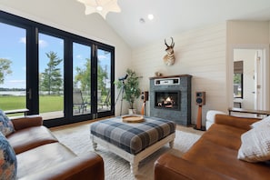 A living room with a fireplace, a large window, and a view of the outdoors. - Pelican Lake Getaway, 2BR + Office, Beach & Pedal Boat (Breezy Point)