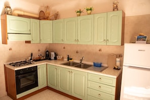 A kitchen with light green cabinets, a gas stove, a sink, and a refrigerator. - La Ca'Setta (La Maddalena)