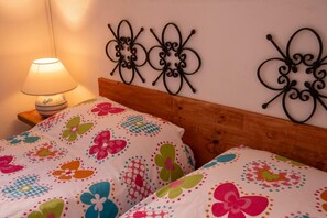 A bed with floral bedding, a wooden headboard, and a wall-mounted decorative metal piece. - La Ca'Setta (La Maddalena)