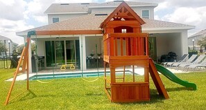 A wooden play structure with a slide and swing set in front of a house with a pool. - 8BR Near Disney Pool, Movie Room, Game Room (Kissimmee)