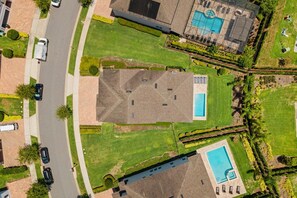 An aerial view of a residential area with a house featuring a swimming pool, a covered patio, and a well-maintained lawn. - 8BR Near Disney Pool, Movie Room, Game Room (Kissimmee)