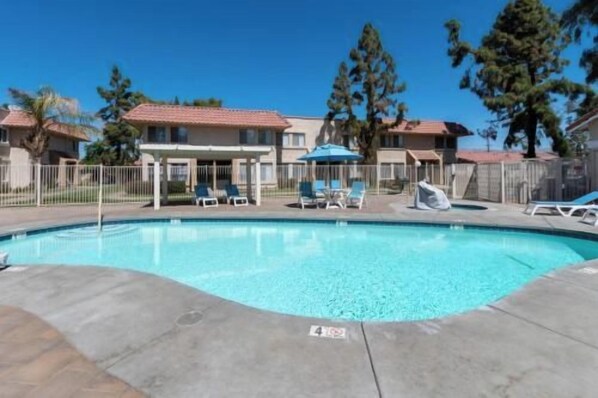 A swimming pool with lounge chairs and umbrellas, surrounded by a fence and trees. - Walk-to-Head-Trip Indio Retreat (Indio)