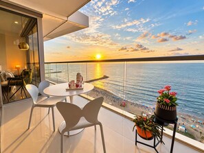 Uma varanda com vista para o mar, uma mesa redonda com cadeiras e plantas em vasos.