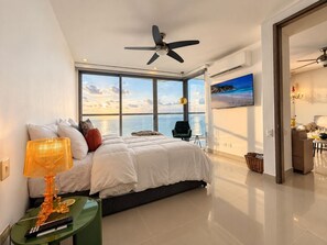 Ein modernes Schlafzimmer mit einem großen Bett, Deckenventilator, Blick zum Himmel und einem Fernseher an der Wand.