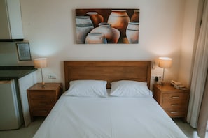 Habitación de hotel con cabecera de madera, cama con ropa blanca, dos mesitas de noche con lámparas, teléfono y un cuadro de jarrones en la pared.