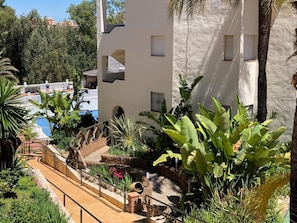 A modern building with a pool, surrounded by lush tropical plants and a wooden staircase. - Crown Resorts (Mijas)