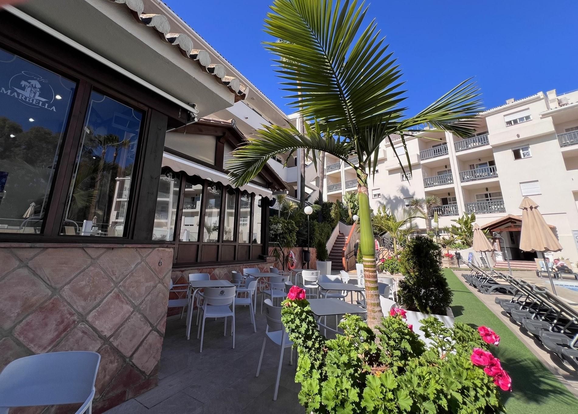 An outdoor seating area with tables and chairs, a palm tree, and a building with balconies.