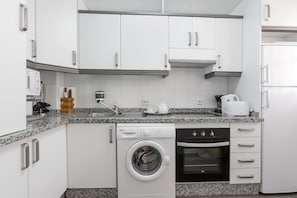 Una cocina moderna con armarios blancos, lavavajillas integrado, lavadora y estufa.