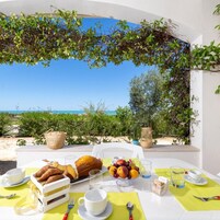 Una tavola imbandita per la colazione con croissant, frutta e caffè, con vista sulla spiaggia.