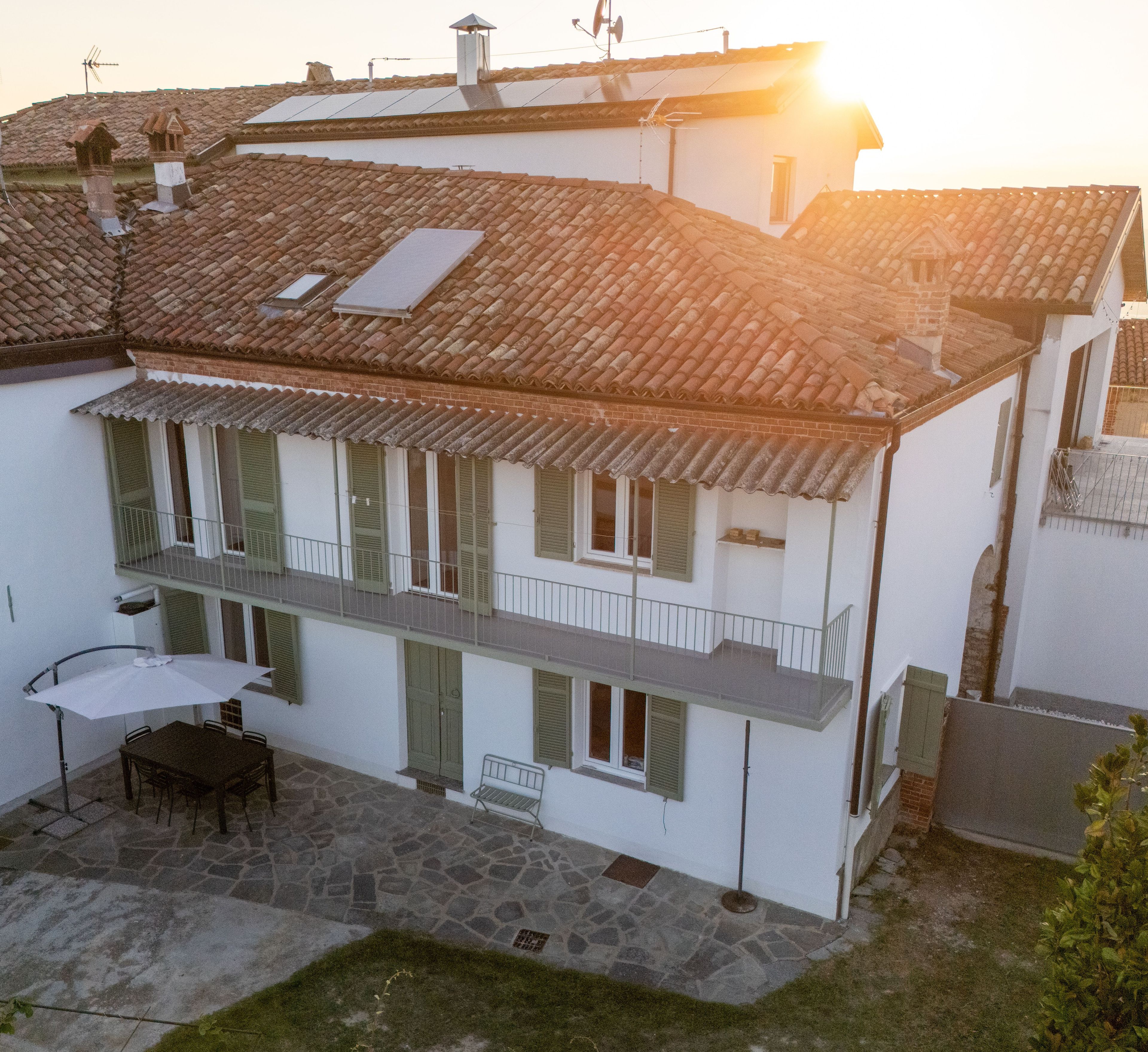 Un edificio a due piani con un balcone, un tavolo con sedie e un cortile soleggiato.