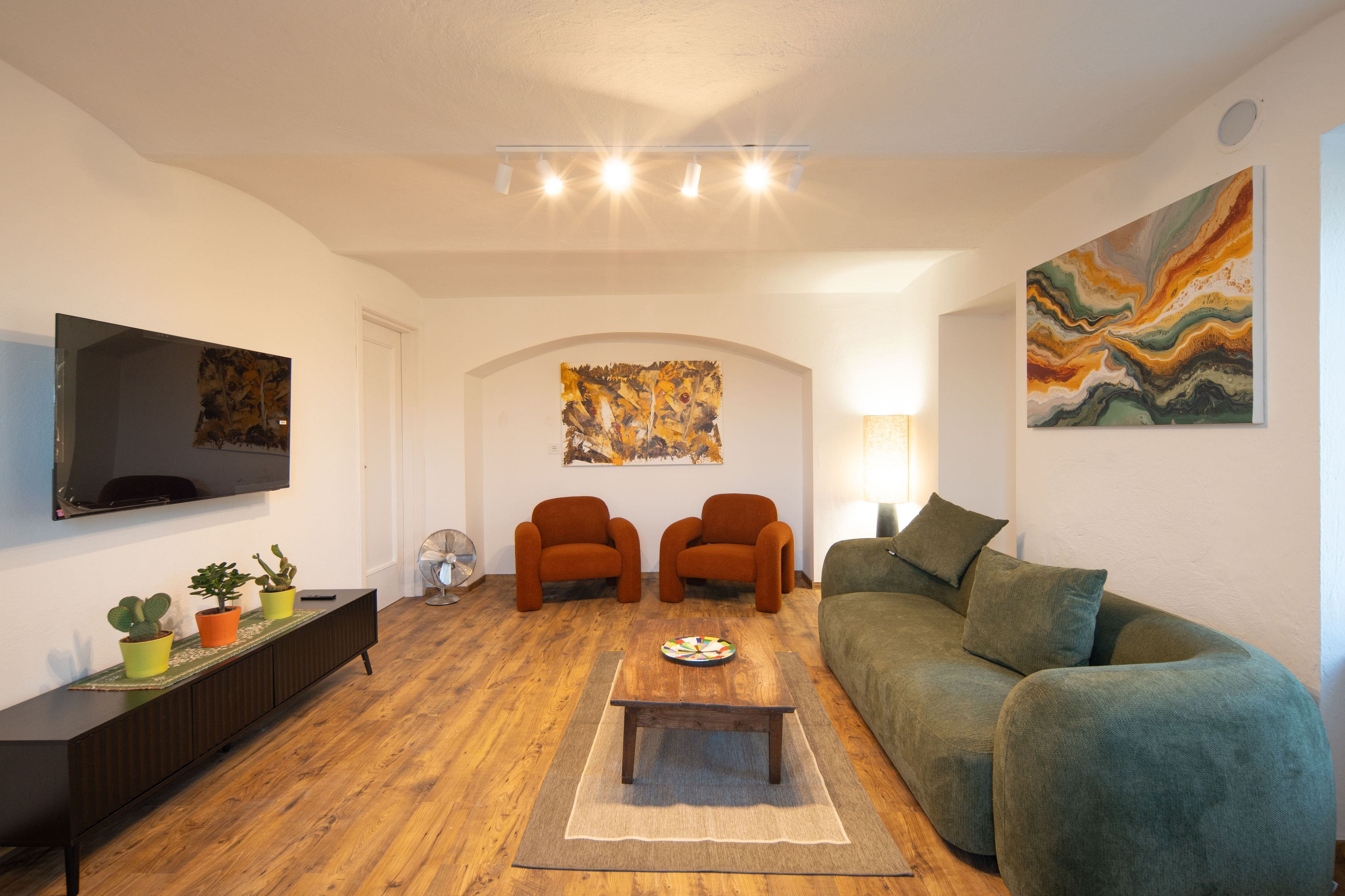 Un salon doté d’un plancher en bois, de deux fauteuils, d’un canapé, d’une table basse, d’un téléviseur à écran plat et d’œuvres d’art accrochées aux murs.