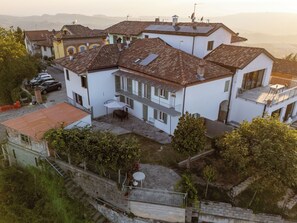 A residential building with multiple levels, a courtyard with a table and chairs, and a staircase leading to an upper level. - Capo d'Alba - Cascina con vista panoramica (Diano d'Alba)
