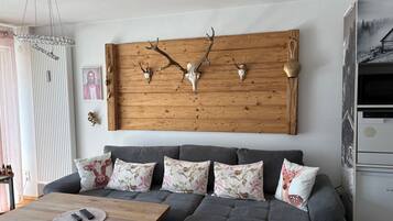 Una sala de estar con un sofá gris, una mesa de centro de madera y un adorno de cabeza de venado en la pared.
