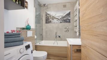 Ein modernes Badezimmer mit Waschmaschine, Toilette, Badewanne und Dusche.