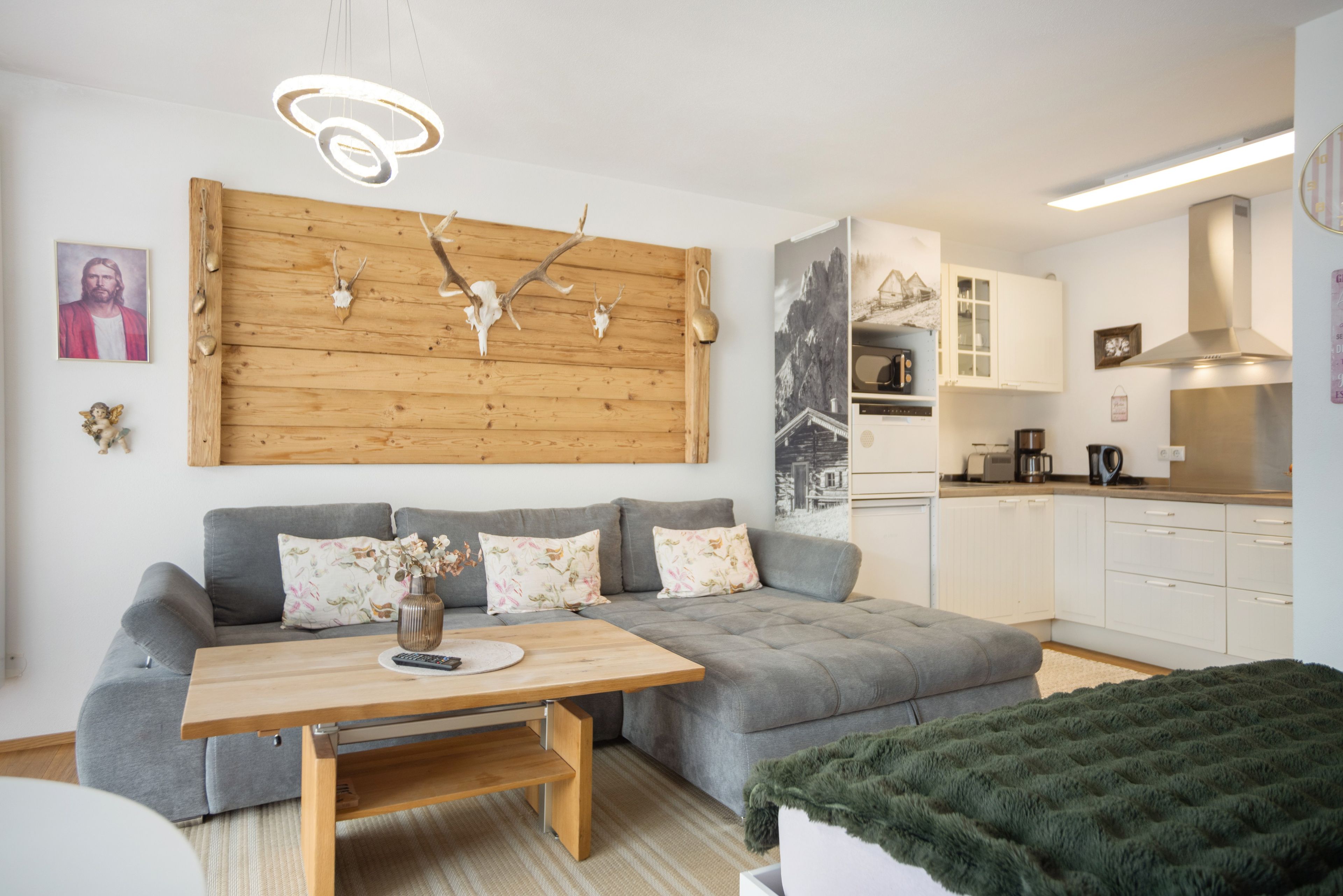 Un salon moderne avec un canapé gris, une table basse en bois et un coin cuisine doté de meubles blancs et d’une cuisinière.