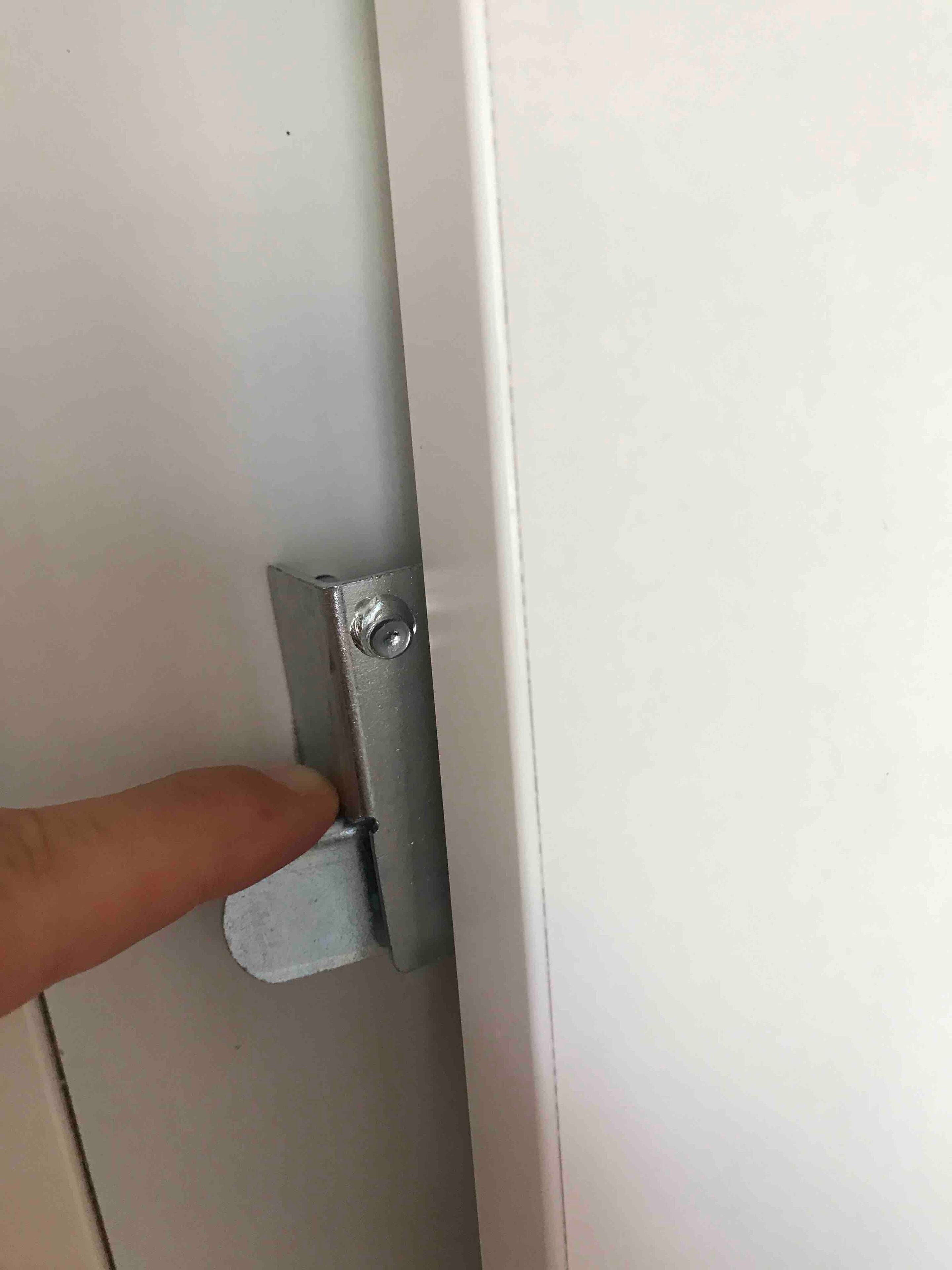 A hand pressing a metallic latch on a white door.