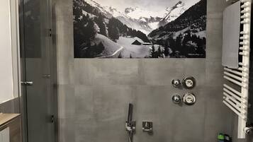 Un baño con un cuadro grande de un paisaje de montaña en blanco y negro, un box de ducha de cristal y una bañera blanca.