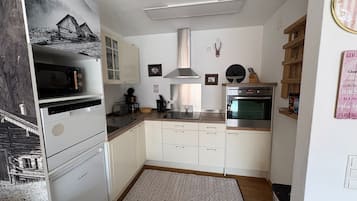 Una cocina compacta con armarios blancos, un refrigerador Bosch, un microondas, una cafetera y un horno empotrado.
