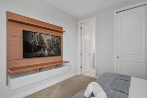 Ein Schlafzimmer mit einem Bett, einem an der Wand befestigten Fernseher, einer Tür und einem Teppichboden.