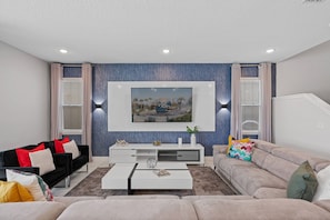 Ein modernes Wohnzimmer mit einem an der Wand befestigten Flachbildfernseher, einem schwarz-roten Sofa, einem beigen Sofa und einem weißen Couchtisch.