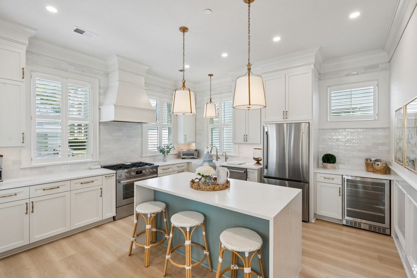 A modern kitchen with white cabinetry, a central island with stools, stainless steel appliances, and pendant lighting.