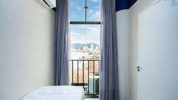 A room with a bed, a window with curtains, and a view of a cityscape.