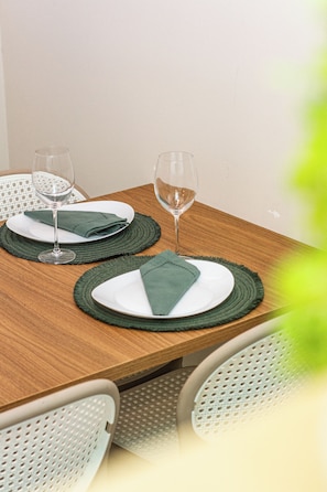 A wooden dining table with two plates, each with a folded napkin and a glass.