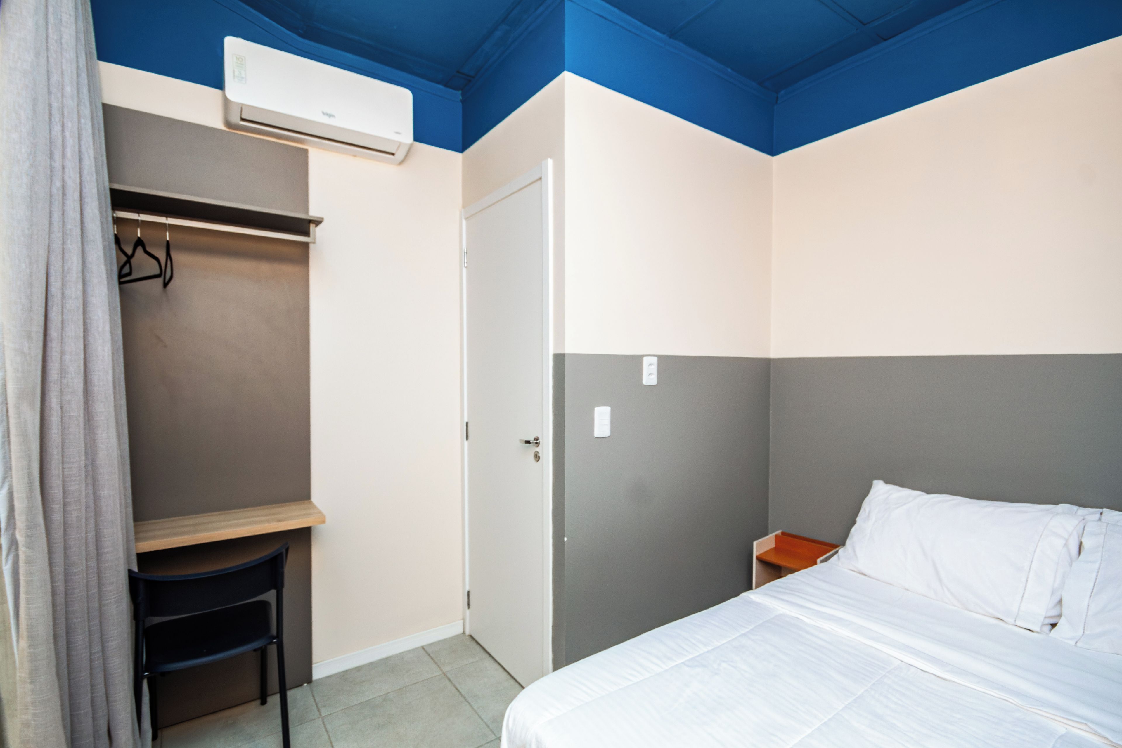 A room with a bed, a wardrobe, a chair, and an air conditioning unit.