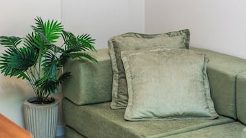 A green sofa with two cushions and a potted plant beside it.