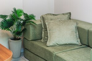 A green sofa with two cushions and a potted plant beside it.