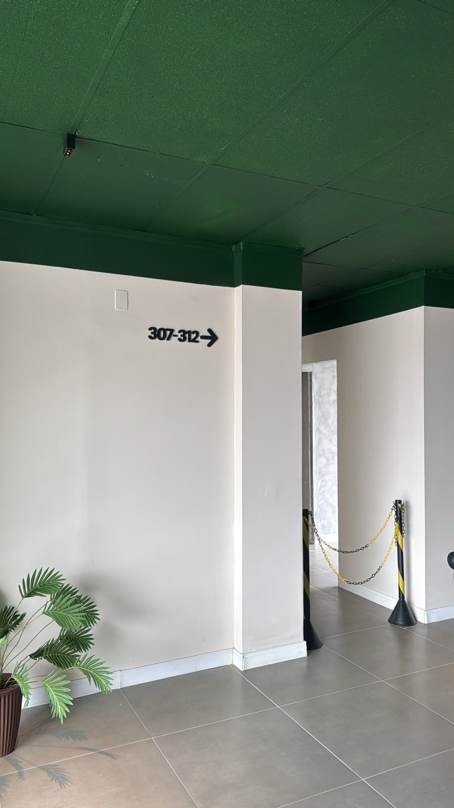 A corridor with directional signage, a potted plant, and a yellow-black barrier.