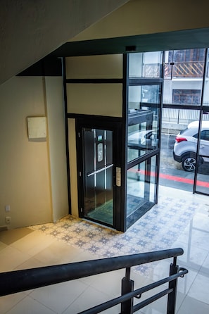 Un ascensor moderno con puertas de vidrio, pasamanos metálico y piso estampado.