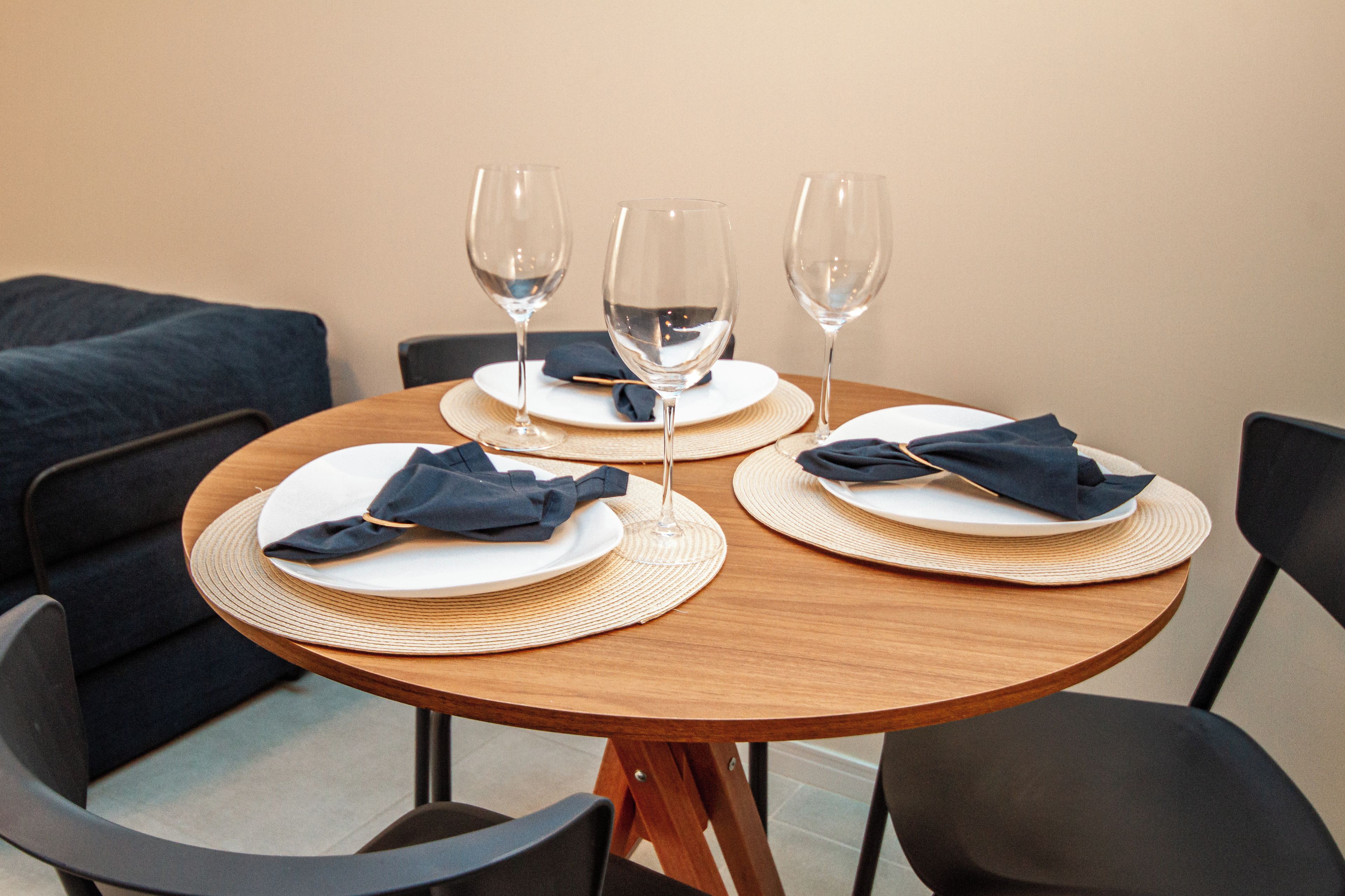 A round dining table with three plates, each with a folded napkin and a glass of water. The table is surrounded by four chairs.