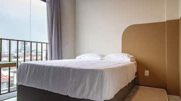 A room with a bed, a small sofa, and a window with a view of buildings.