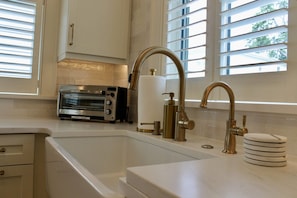 A kitchen with a built-in toaster oven, a stainless steel sink with a gold faucet, and a window with blinds. - The Bower House- Walk to King! (Charleston)