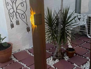 A potted plant, a wooden post, and a wall-mounted light fixture. - RAS Casita Encanto (West Palm Beach)