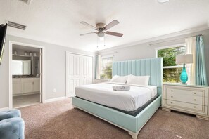 Een slaapkamer met een bed, een nachtkastje, een dressoir, een plafondventilator en een raam met gordijnen.
