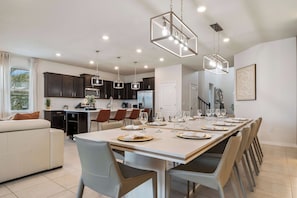 A modern kitchen with dark cabinets, a dining area with a long table set for six, and a living area with a sofa. - Disney Dream Home Mario, Frozen & Minions (Davenport)