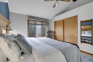 A bedroom with a bed, a wooden wardrobe, a window with a view of trees, and a ceiling fan. - Private Hot Tub | Game Room | Waterville Valley (Campton)