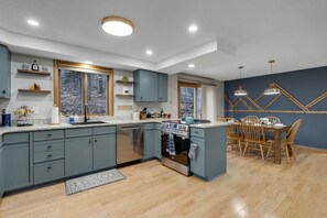 A modern kitchen with grey cabinets, a central island, and a dining area with wooden chairs. - Private Hot Tub | Game Room | Waterville Valley (Campton)