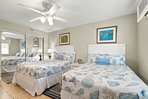 A hotel room with two beds, a ceiling fan, a large mirror, and a framed picture on the wall. - Sand Castle Oceanfront Condo (Indian Shores)
