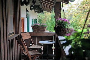 A wooden porch with a table and chairs, a hanging basket with flowers, and a view of greenery. - "TENNE" Loft Apartment at the WEBERHOF - A Stylish Getaway with a Rural Charm (Feldkirchen-Westerham)