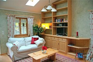 Ein gemütliches Wohnzimmer mit einer Couch, einem Couchtisch aus Holz, einem Fernseher und einem Bücherregal.