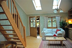 Una habitación con escaleras de madera, un sofá, una mesita de centro y una ventana con cortinas.