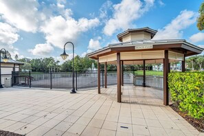 A covered pavilion with a sign reading 'BEACH CLUB' and a fenced area with a fountain. - 2BR Condo Near Disney Resort Pool (Kissimmee)