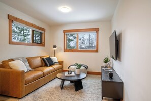 A living room with a brown leather sofa, a round coffee table, and a TV mounted on the wall. - Aspen Adventure House  (Revelstoke)