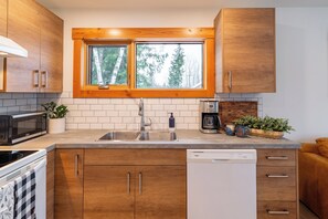 A modern kitchen with wooden cabinets, a double sink, a microwave, a coffee maker, and a dishwasher.