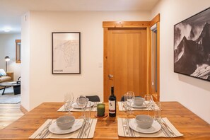 A dining area with a wooden table set for four, a framed map on the wall, and a mountain view painting. - Aspen Adventure House  (Revelstoke)